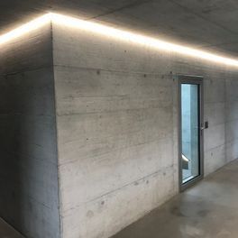Un couloir avec un mur en béton et une porte vitrée.