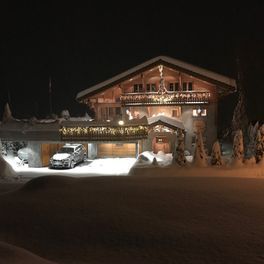 Une voiture est garée devant une maison dans la neige la nuit.