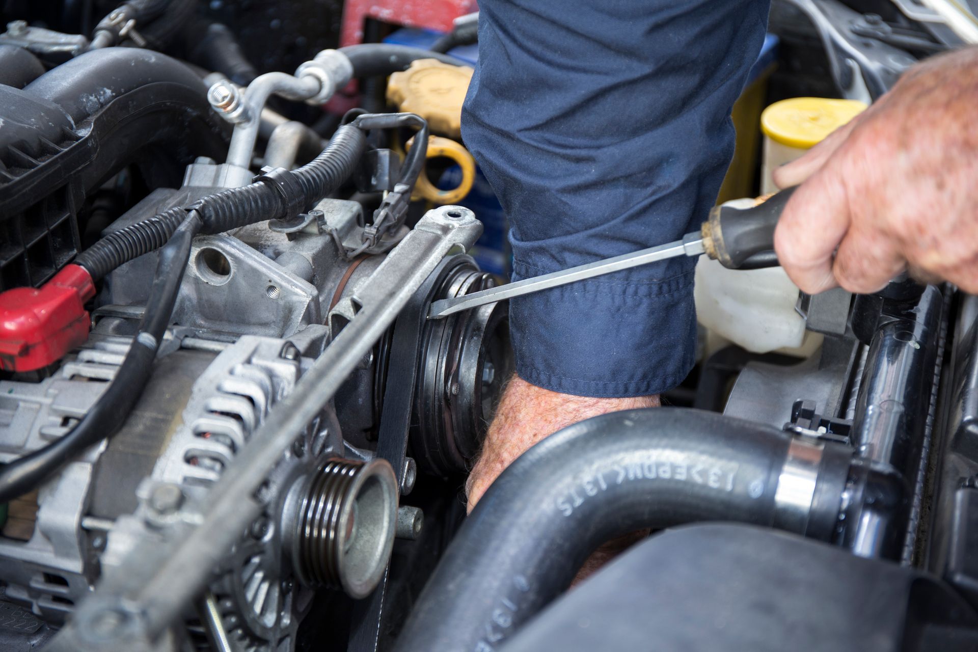A man is working on a car engine with a screwdriver.