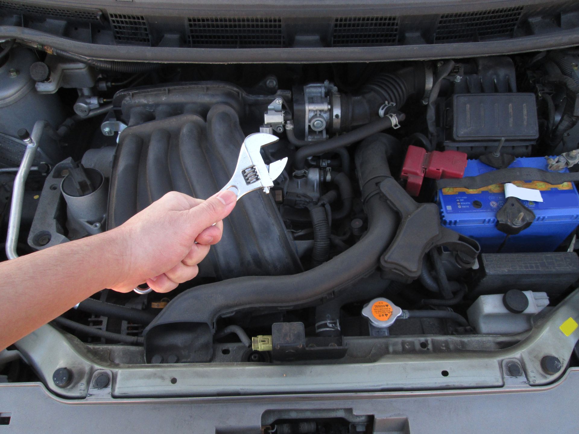 A person is working on the engine of a car with a wrench.
