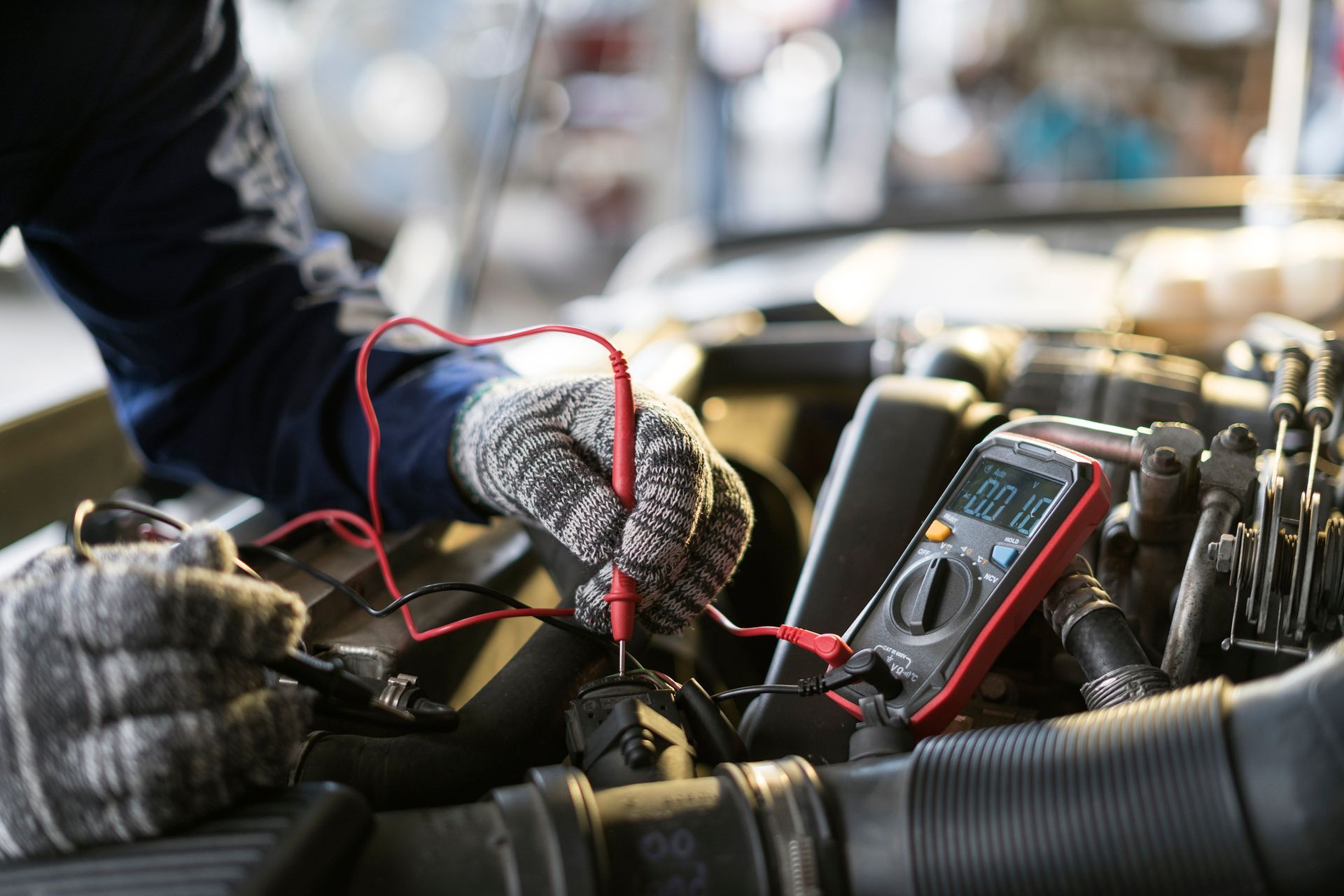 A mechanic is working on a car engine with a multimeter.
