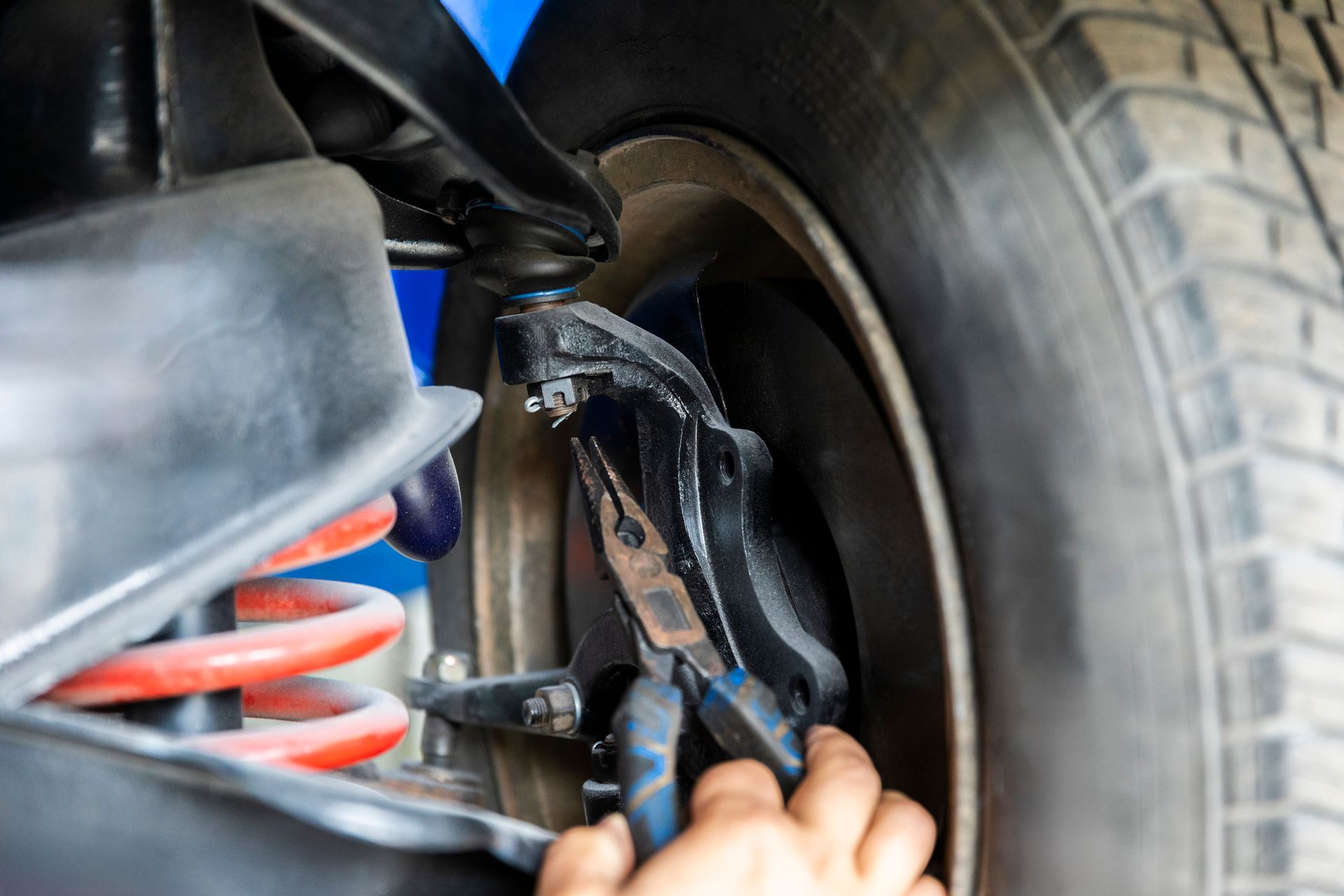 A person is working on the suspension of a car with pliers.