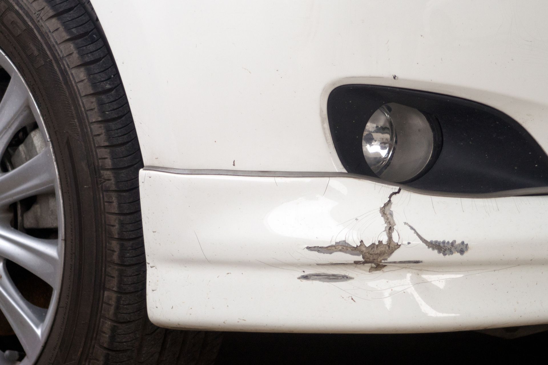 A close up of a white car with a damaged bumper.