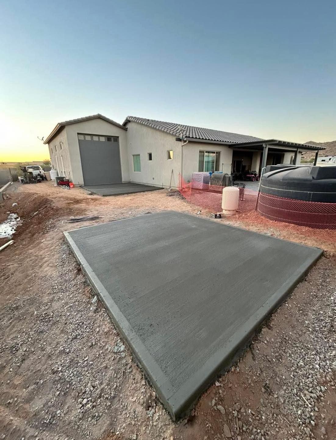 Newly poured concrete pad in front of a house. Gravel, sky. Garage door.
