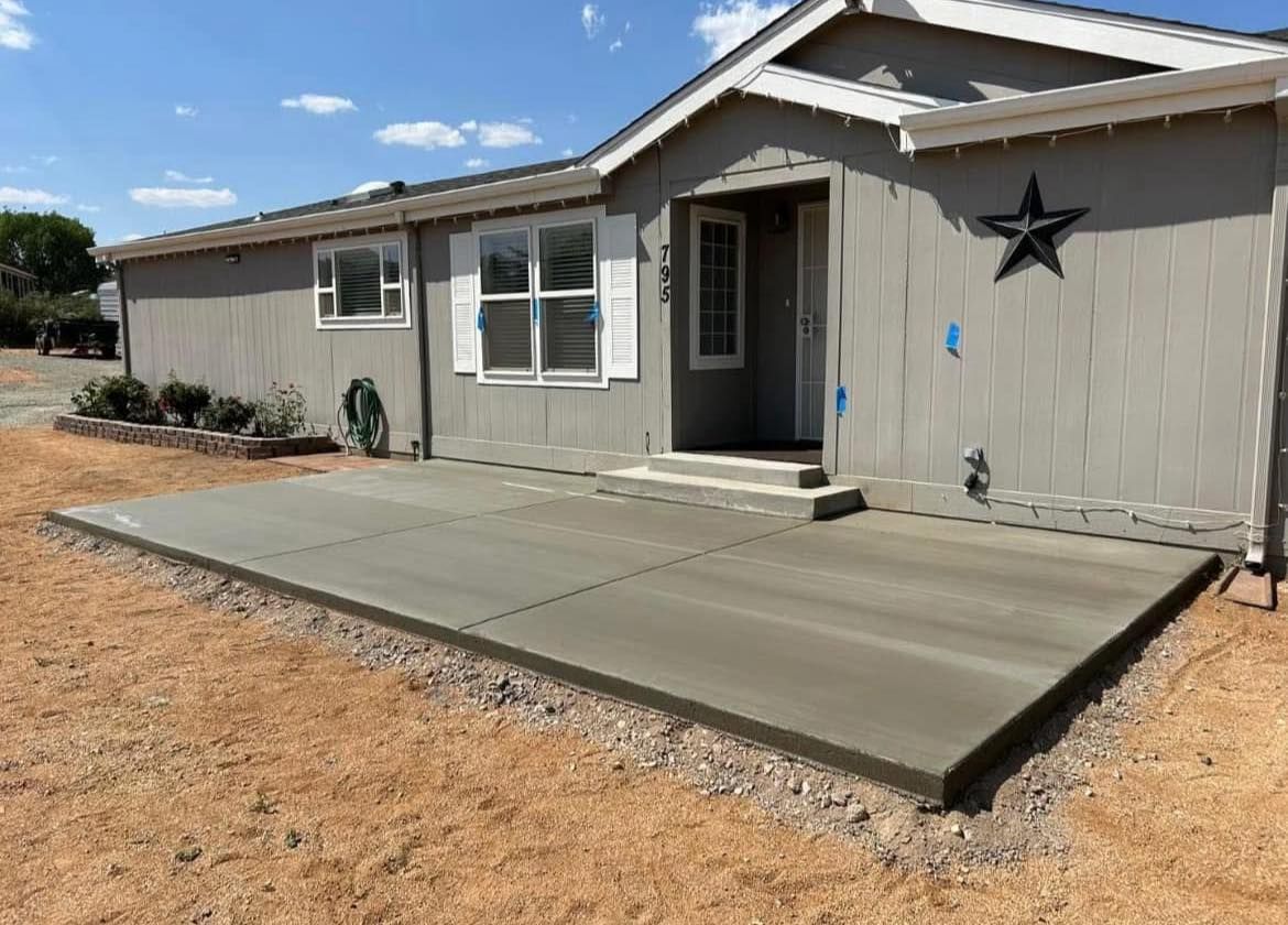 Gray concrete patio in front of a gray house with a star decoration, set in a dry, dirt landscape.