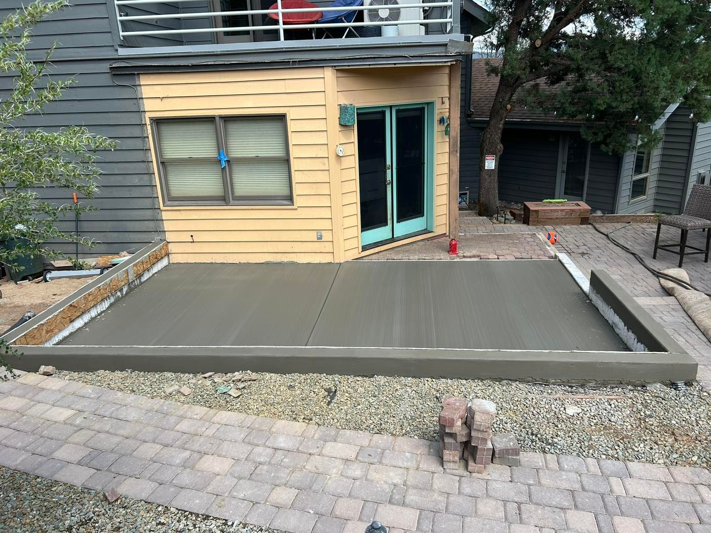 New concrete patio next to a house with pebble walkway.