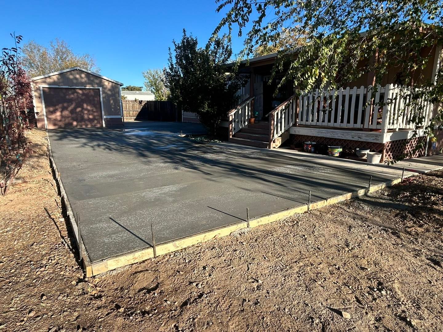 Freshly poured concrete driveway in front of a house and garage; wooden edging, sunny outdoor setting.