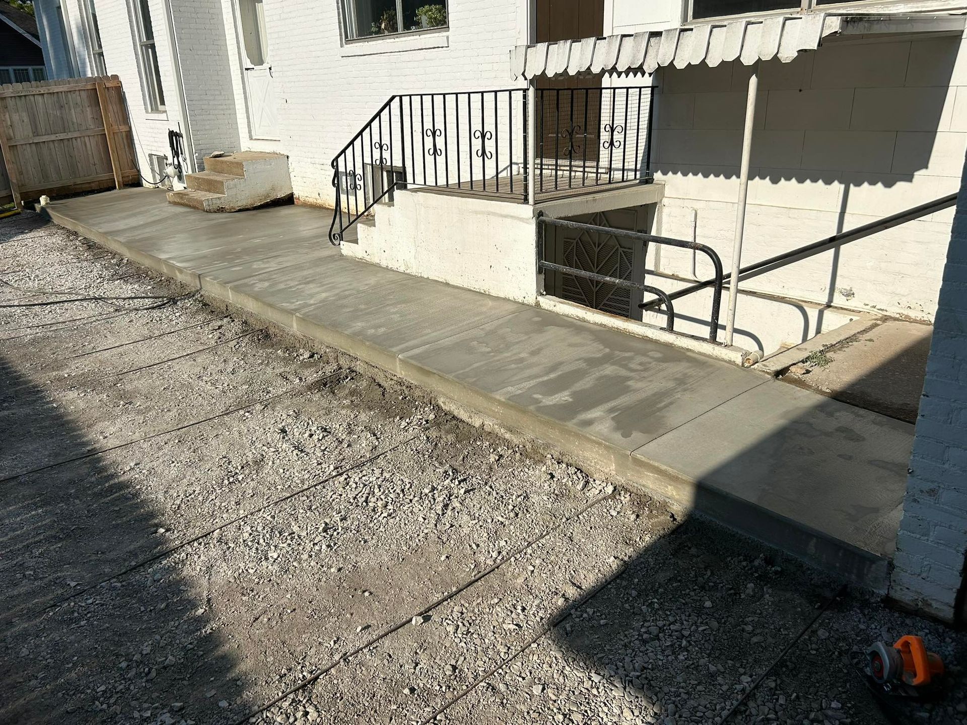 Concrete ramp leading to a building with a black railing, gravel ground.