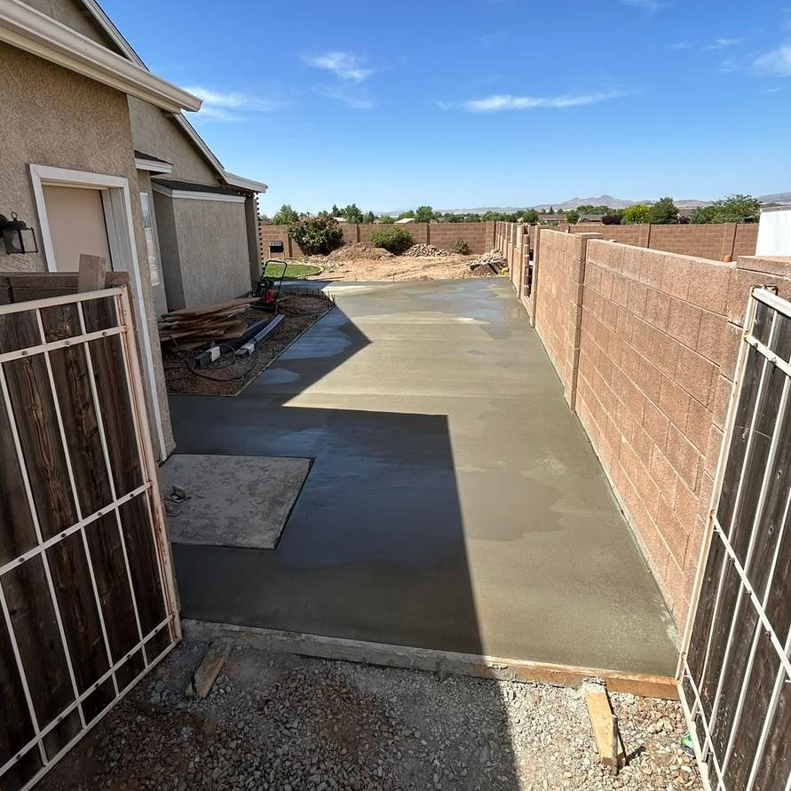 Newly poured concrete patio between a house and brick walls, under a blue sky.
