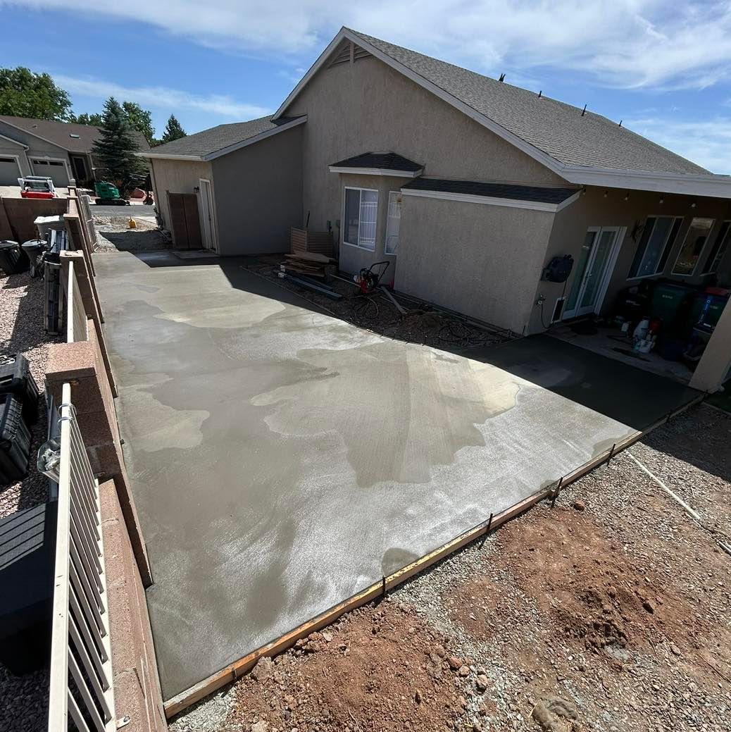 Freshly poured concrete patio next to a house with a tan exterior and a gray roof.