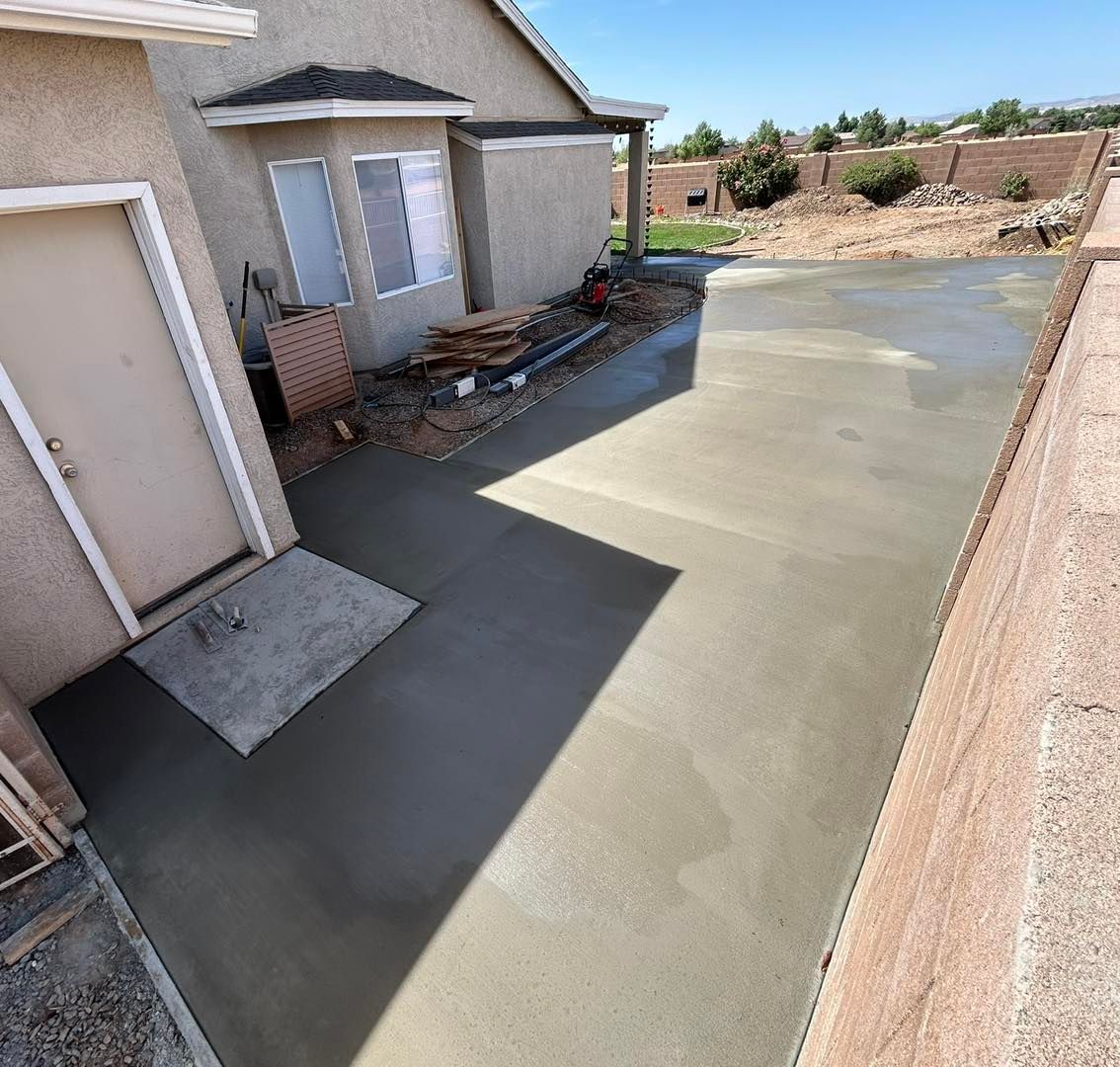Newly poured concrete patio next to a house with a garage door and window.