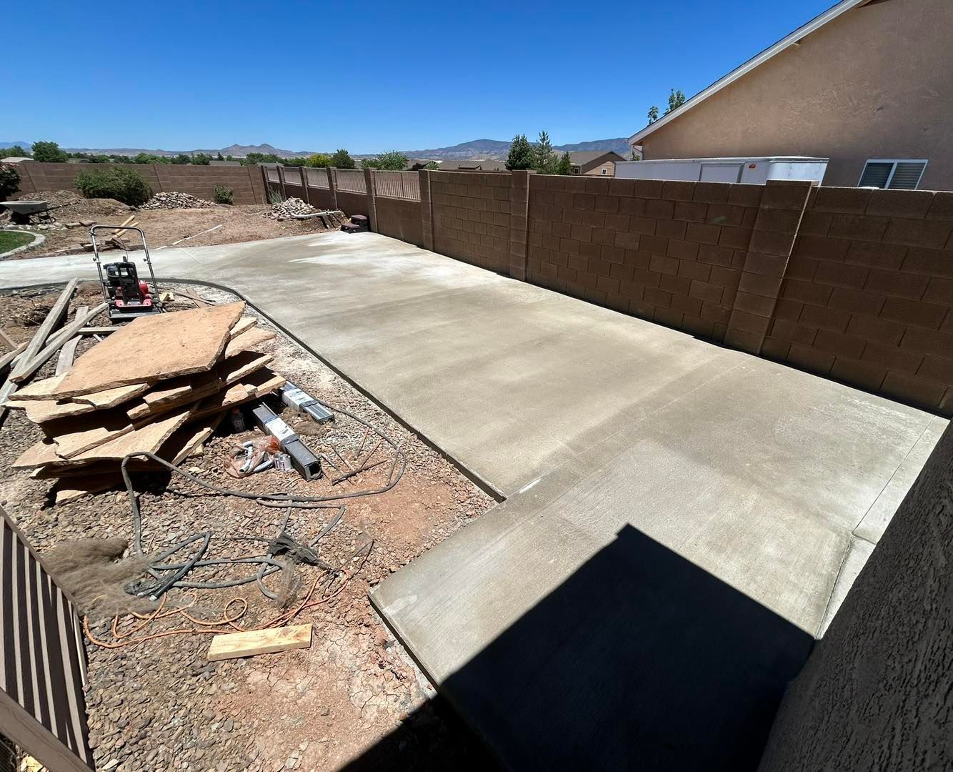 Newly poured concrete patio in a backyard with a brick wall.