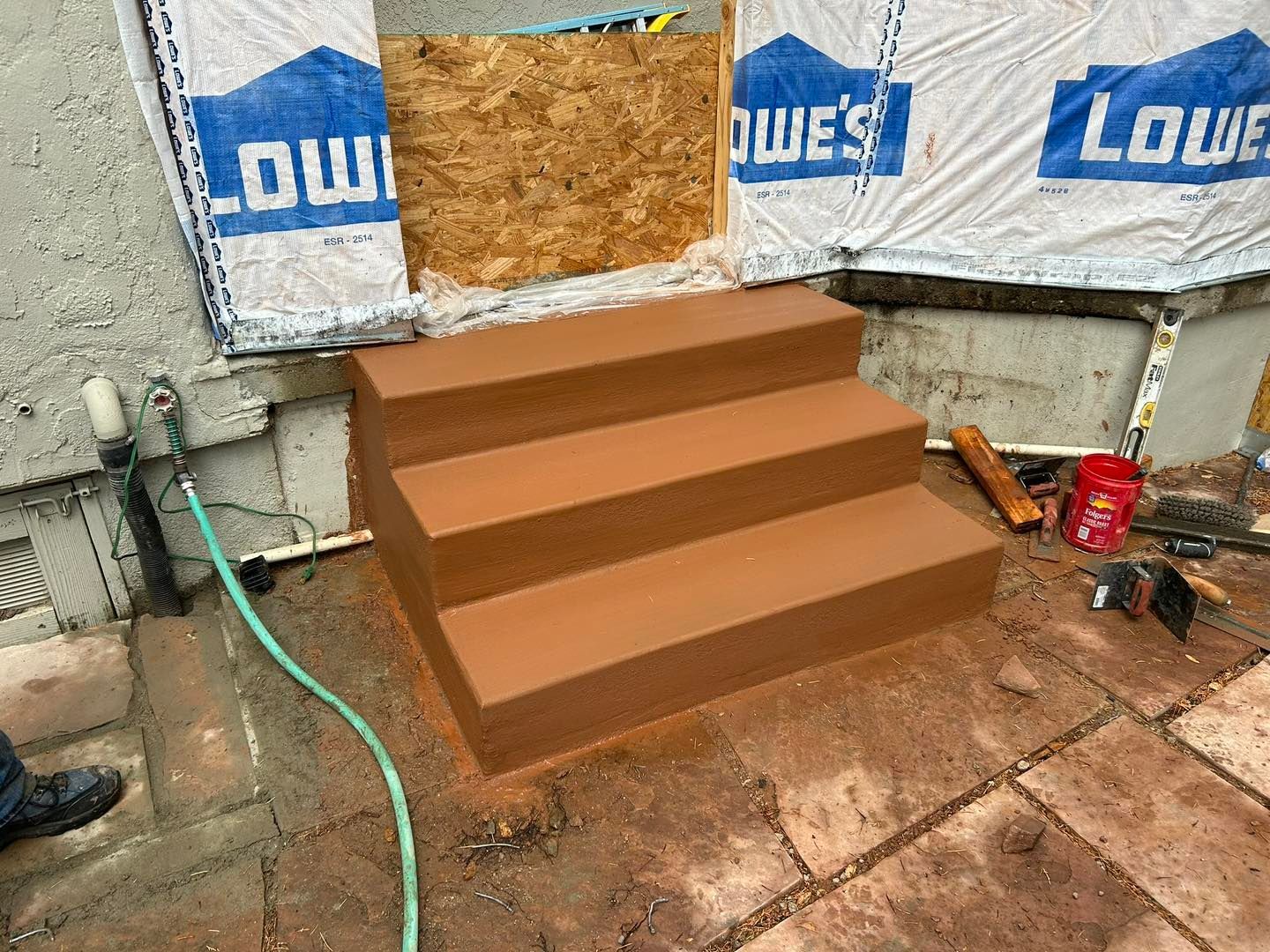 Brown concrete steps in front of a doorway under construction, with Lowe's wrap visible.