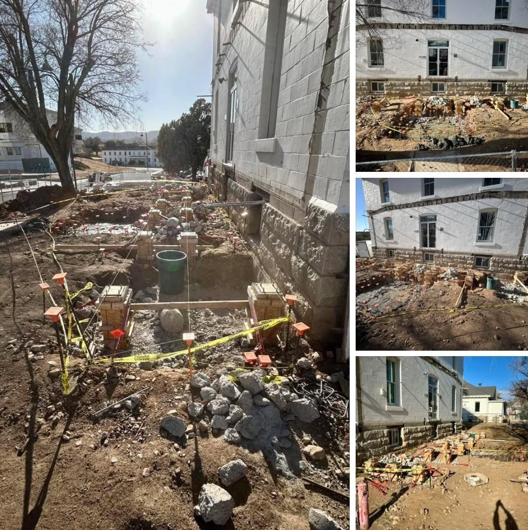 Building foundation repair: workers excavating around a white building's foundation, using tools and caution tape.