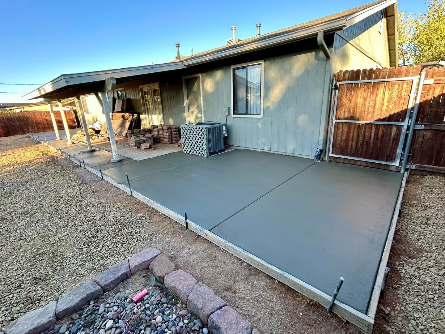 Newly poured concrete patio next to a house with a wooden fence and gravel yard.