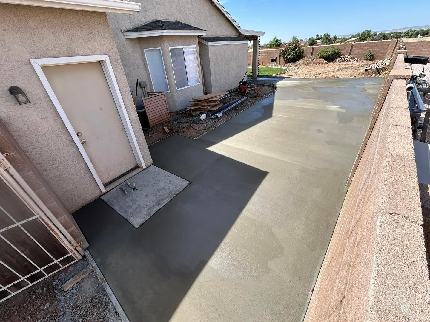Newly poured concrete patio next to a house with a door, window, and low wall.