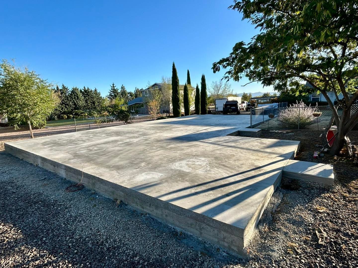 A concrete slab in an outdoor setting, surrounded by gravel and trees, under a blue sky.