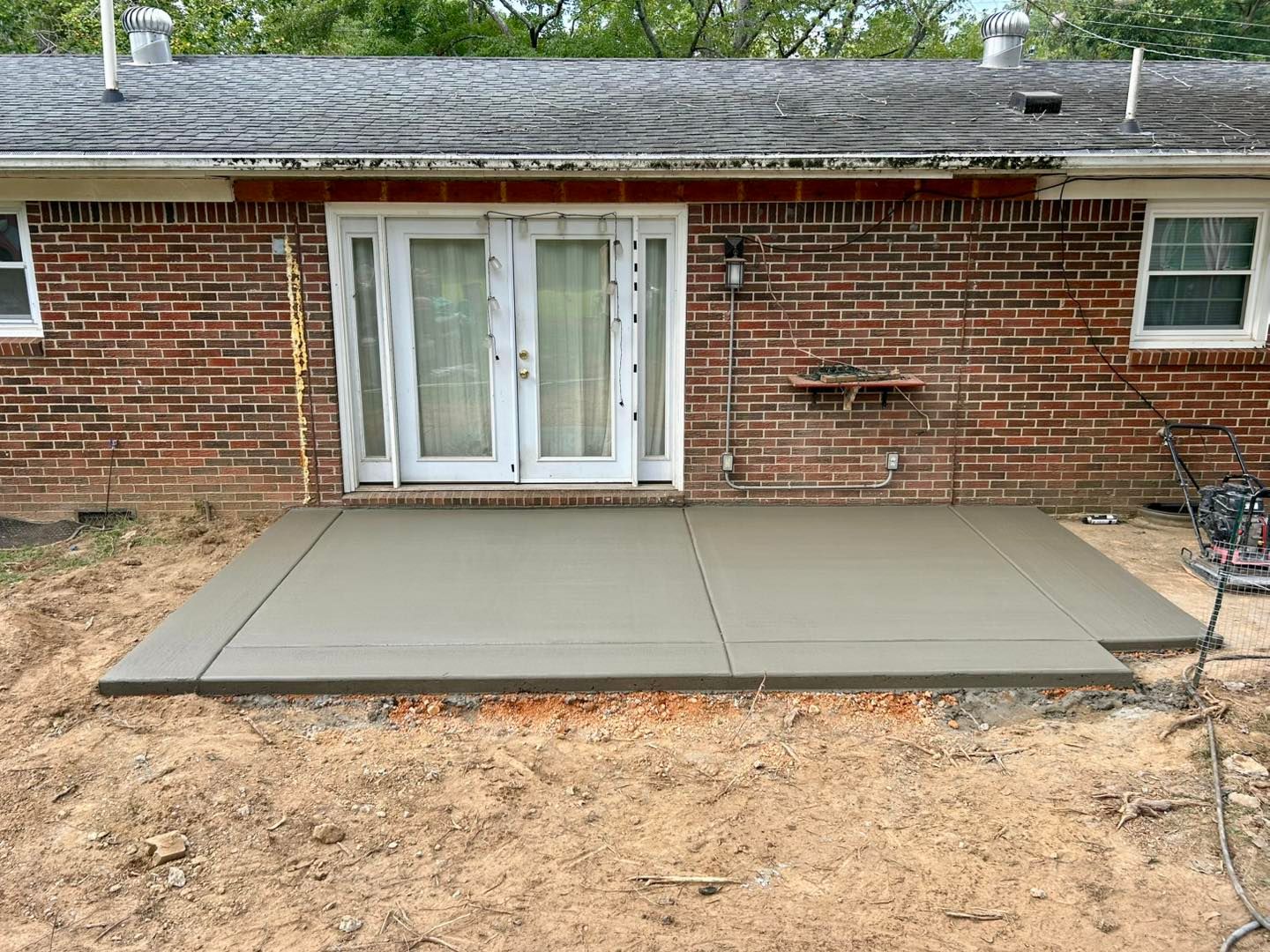 Freshly poured concrete patio in front of a brick house with white double doors.