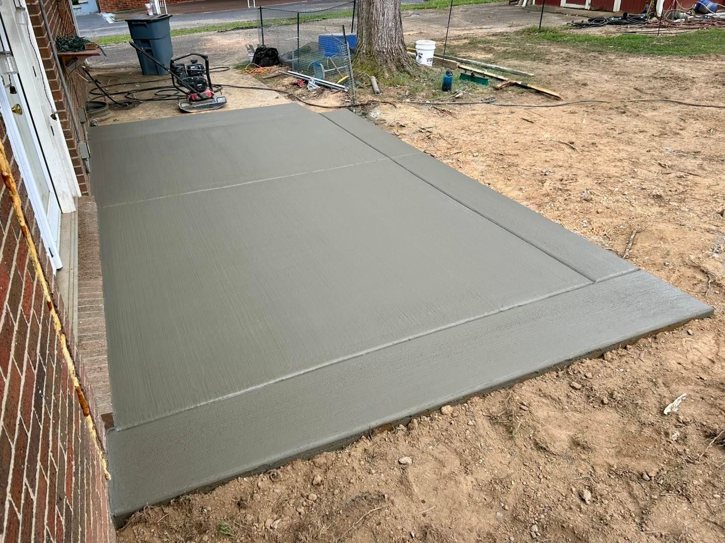 Newly poured concrete patio next to a brick building, with a finished border and unfinished yard.