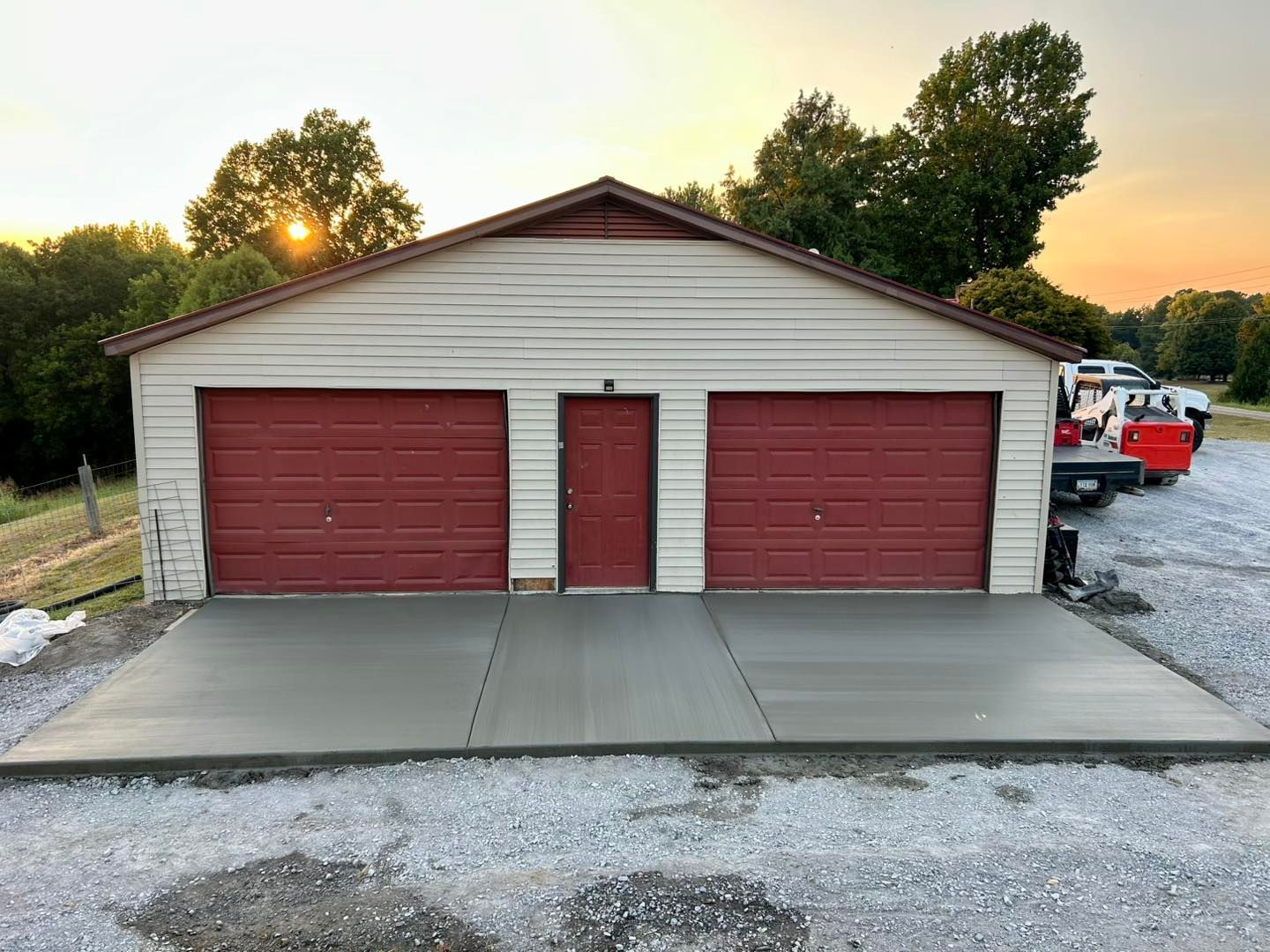 Two-car garage with red doors and a newly poured concrete driveway at sunset.