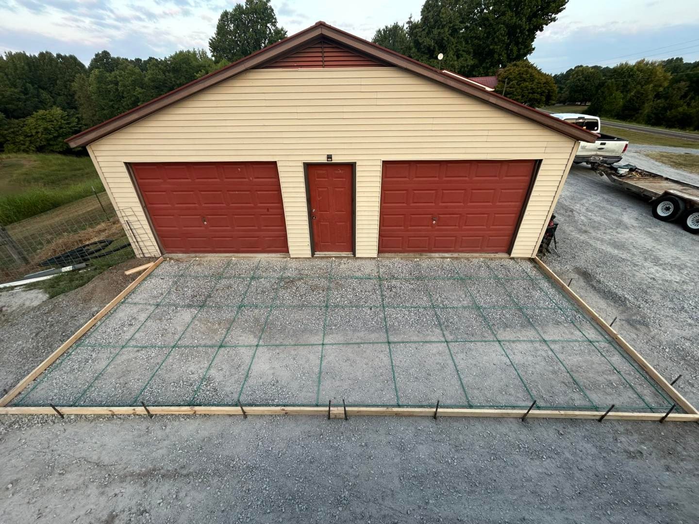 Garage with red doors, a new concrete slab in front, and a gravel driveway.