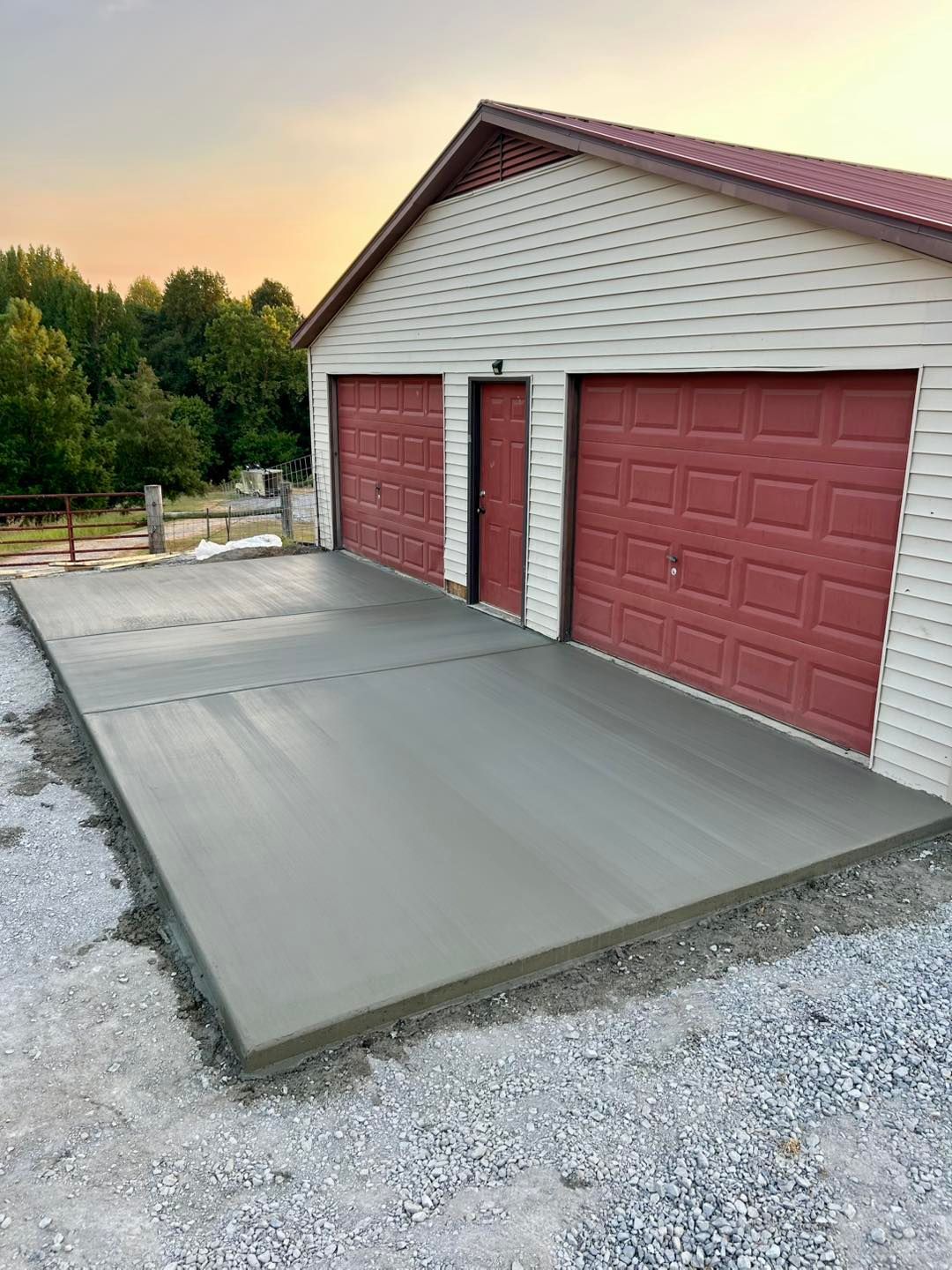 Newly poured concrete driveway in front of a two-car garage with red doors and siding.