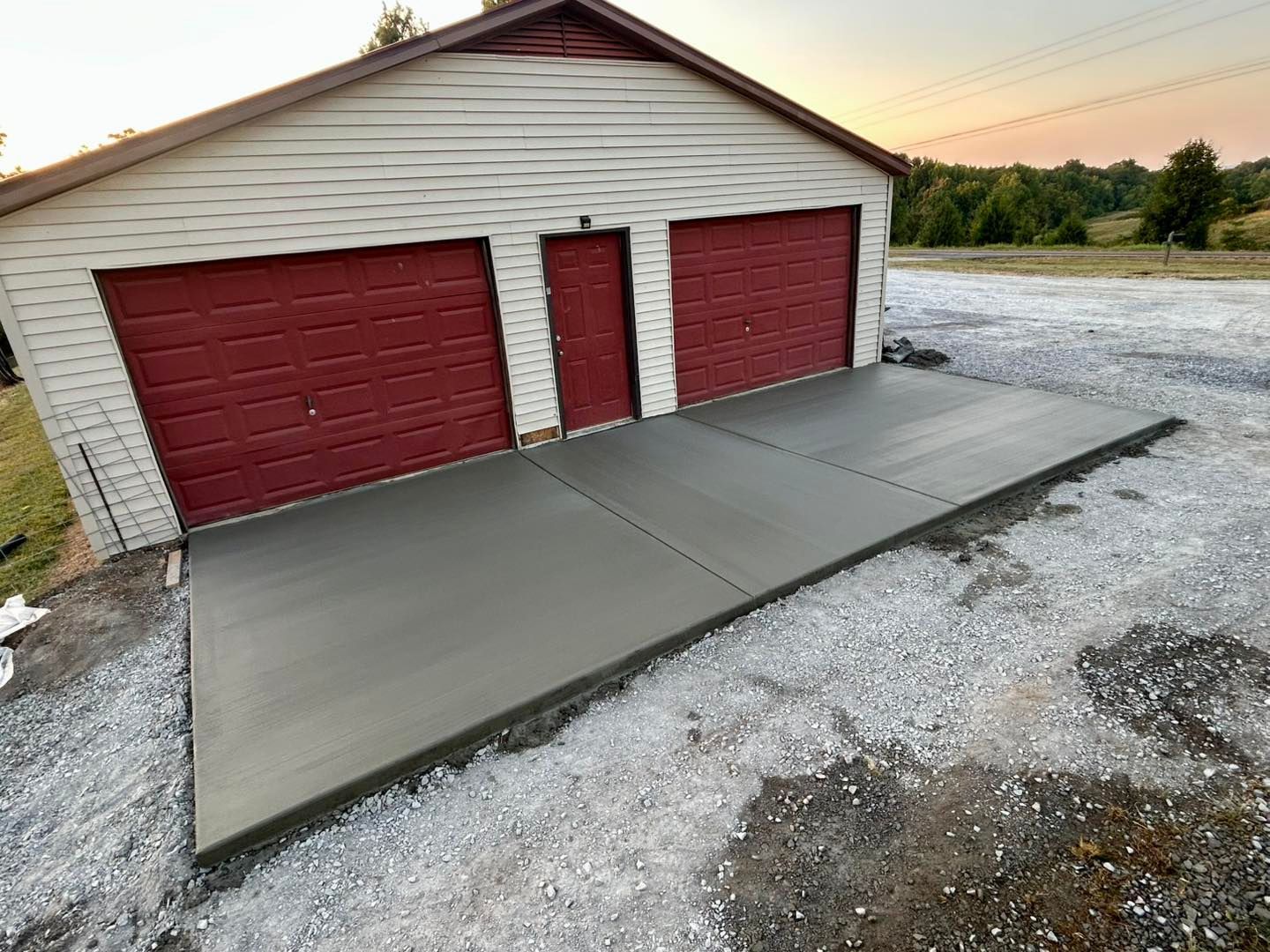 Freshly poured concrete driveway in front of a two-car garage with red doors.