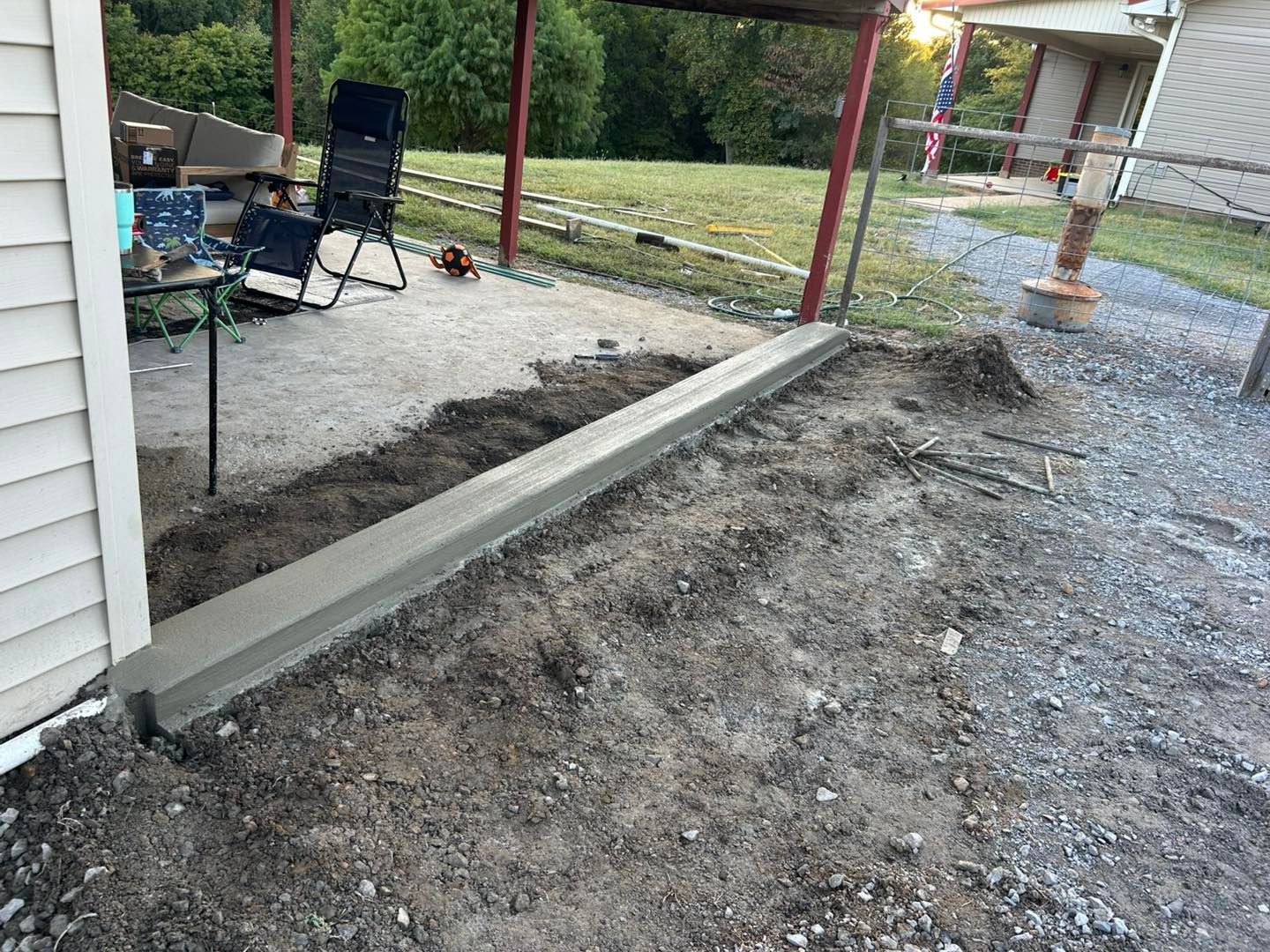Concrete curb along a dirt path, next to a building. An open-air structure is in the background.