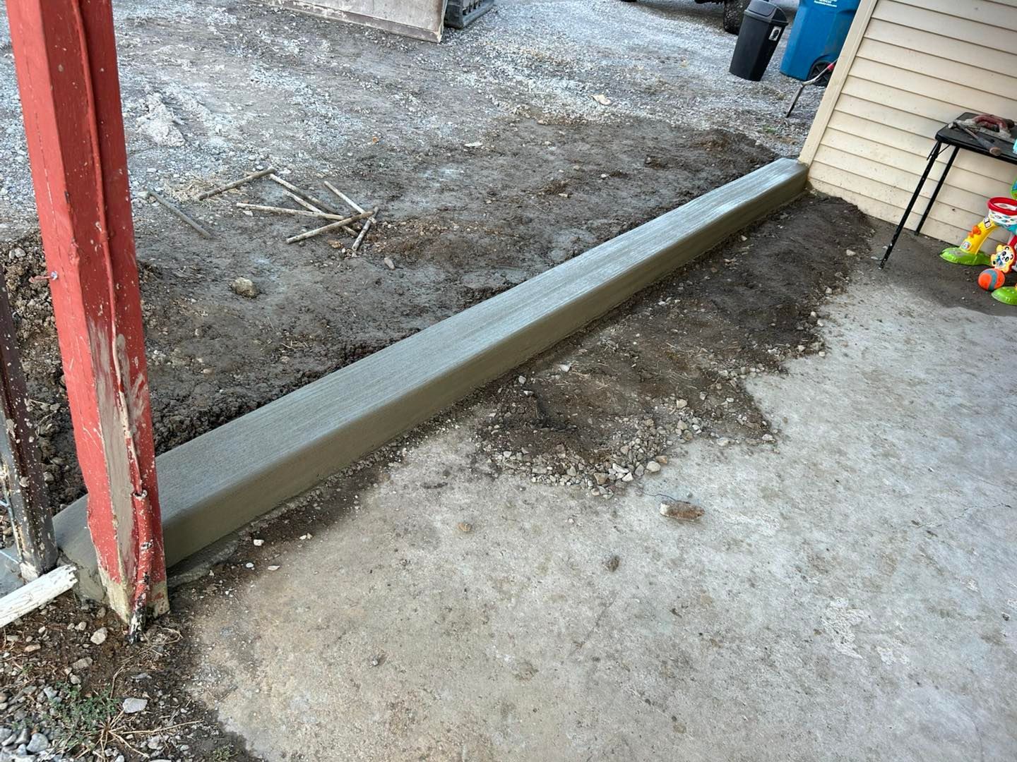 A long concrete curb next to a building and a weathered wooden post, outdoors.