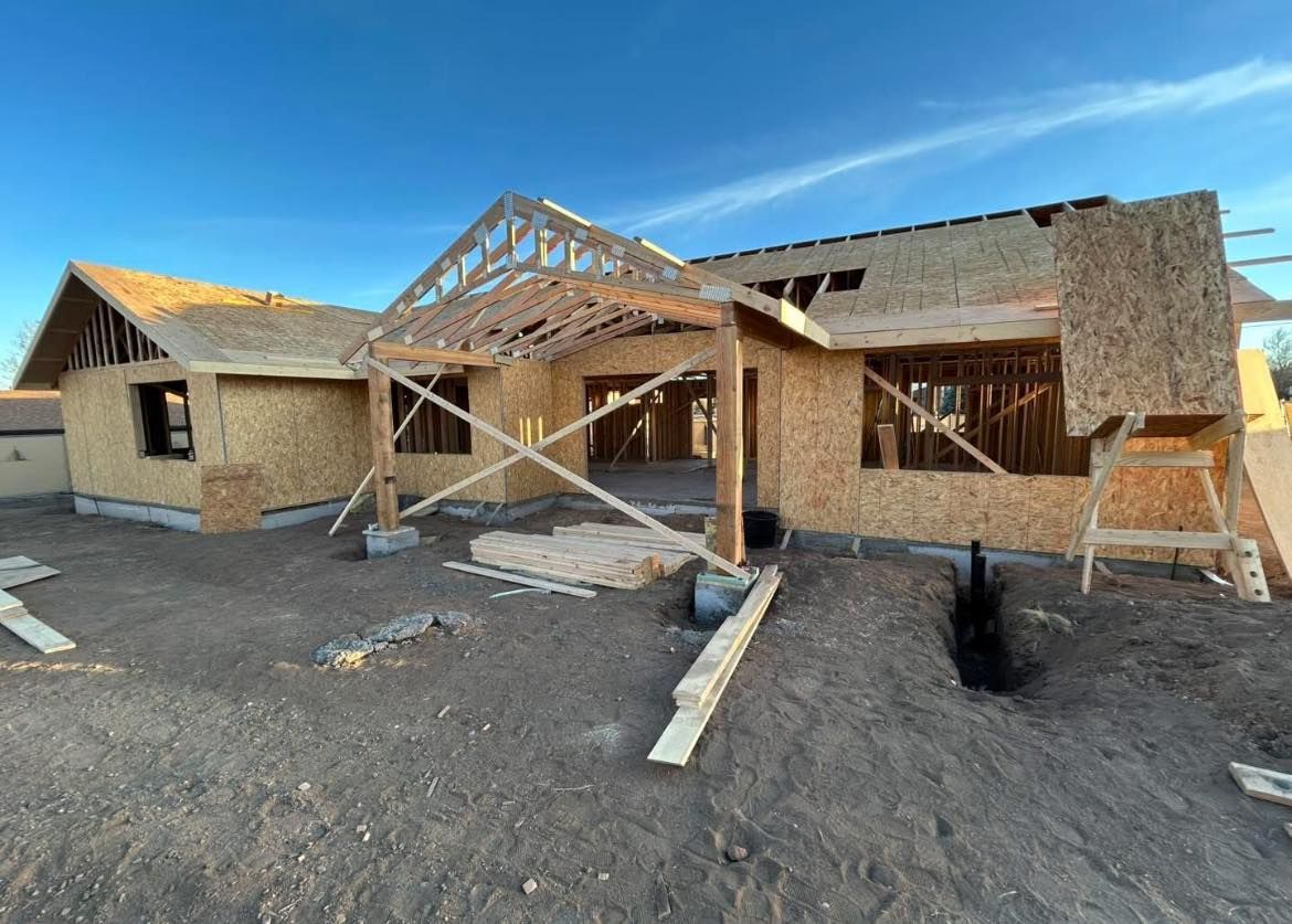 Construction of a house with exposed wooden framing and OSB siding; outdoors, under a blue sky.