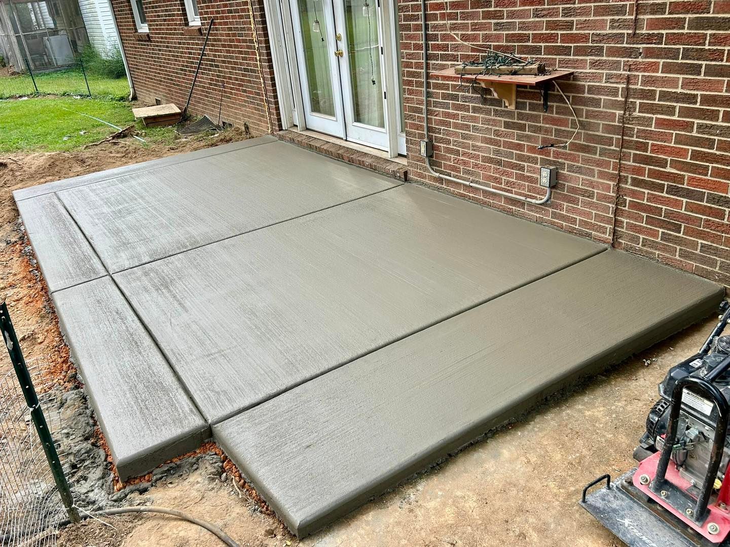Newly poured concrete patio next to a brick building.