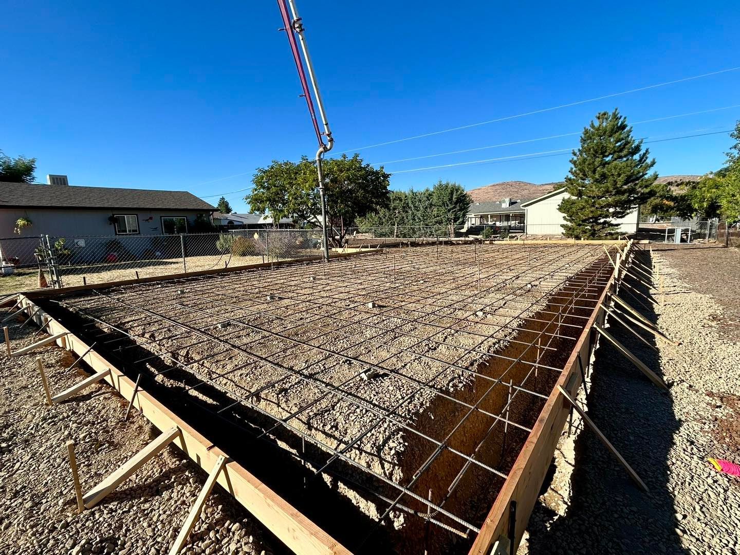 Construction site with concrete forms and rebar, ready for pouring. Gravel base, pump truck overhead, sunny outdoors.