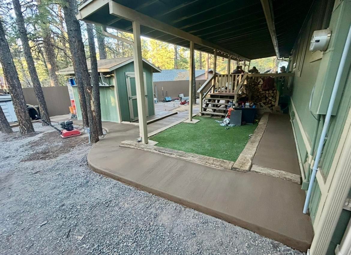 A covered porch and walkway beside a building, with a small green shed and artificial turf.