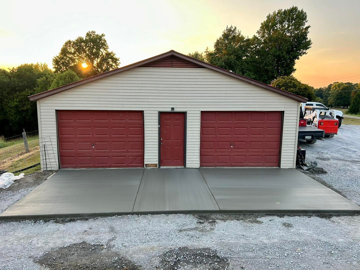 Two-car garage with red doors and a newly poured concrete driveway at sunset.