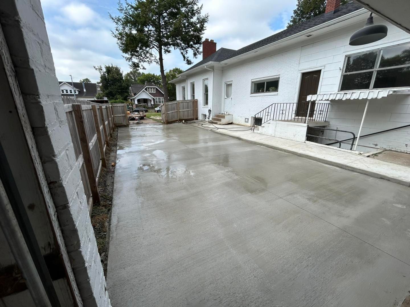 Newly poured concrete driveway next to a white house and wooden fence.