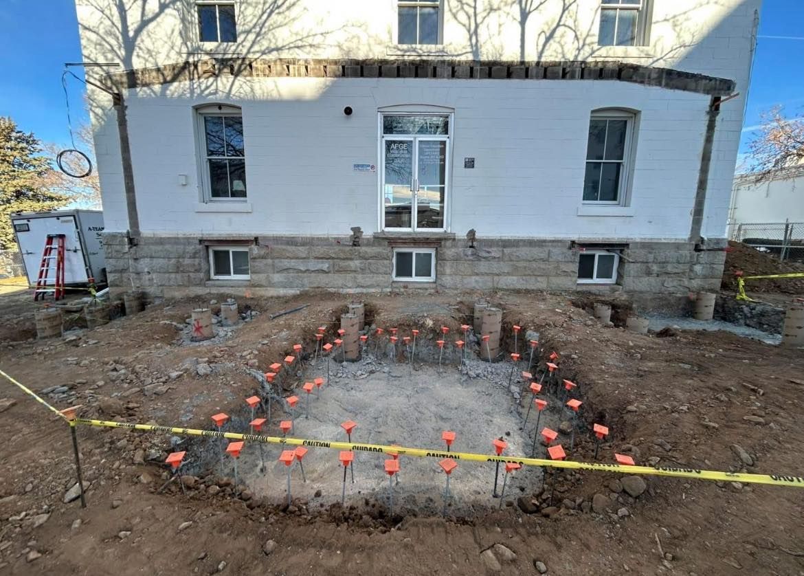 Building foundation excavation with orange markers and caution tape.