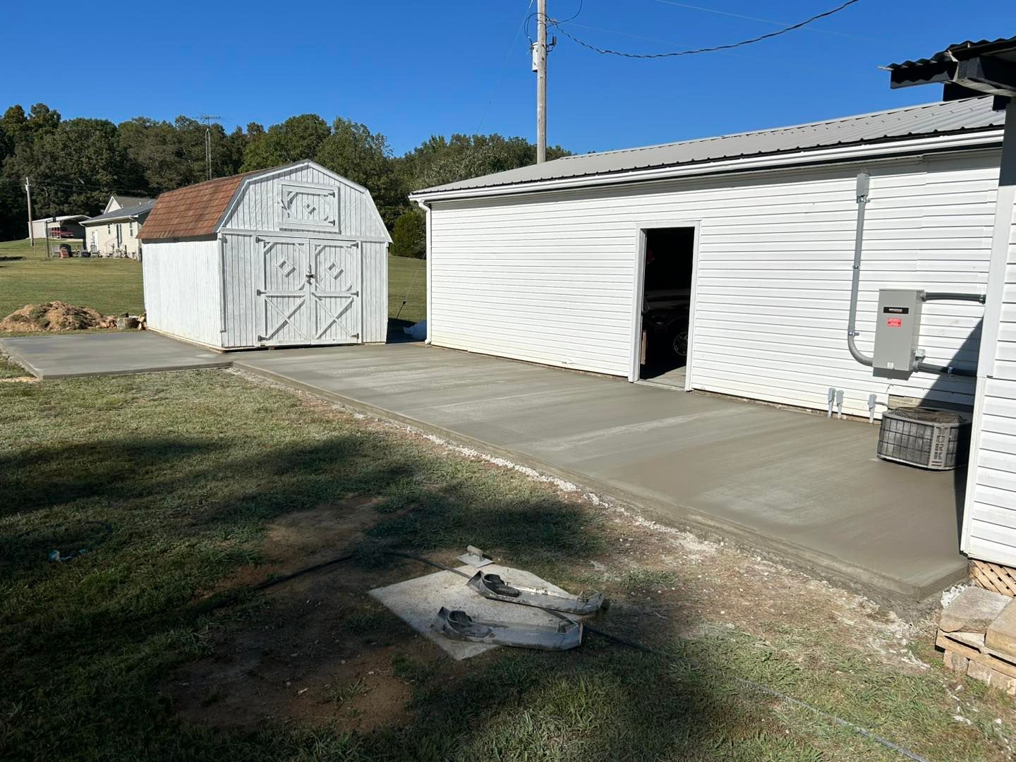 New concrete patio next to a white building with an open door; shed in the background.