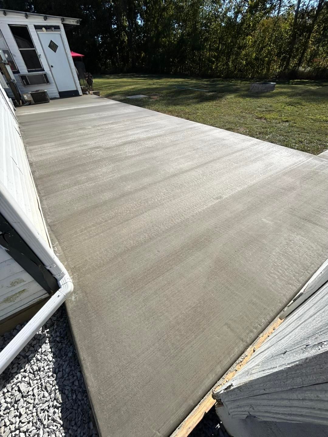 Newly poured concrete pathway leading to a building's white door, set in a grassy yard.