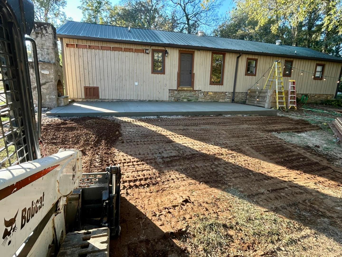 Bobcat grading dirt in front of a building with a concrete patio.