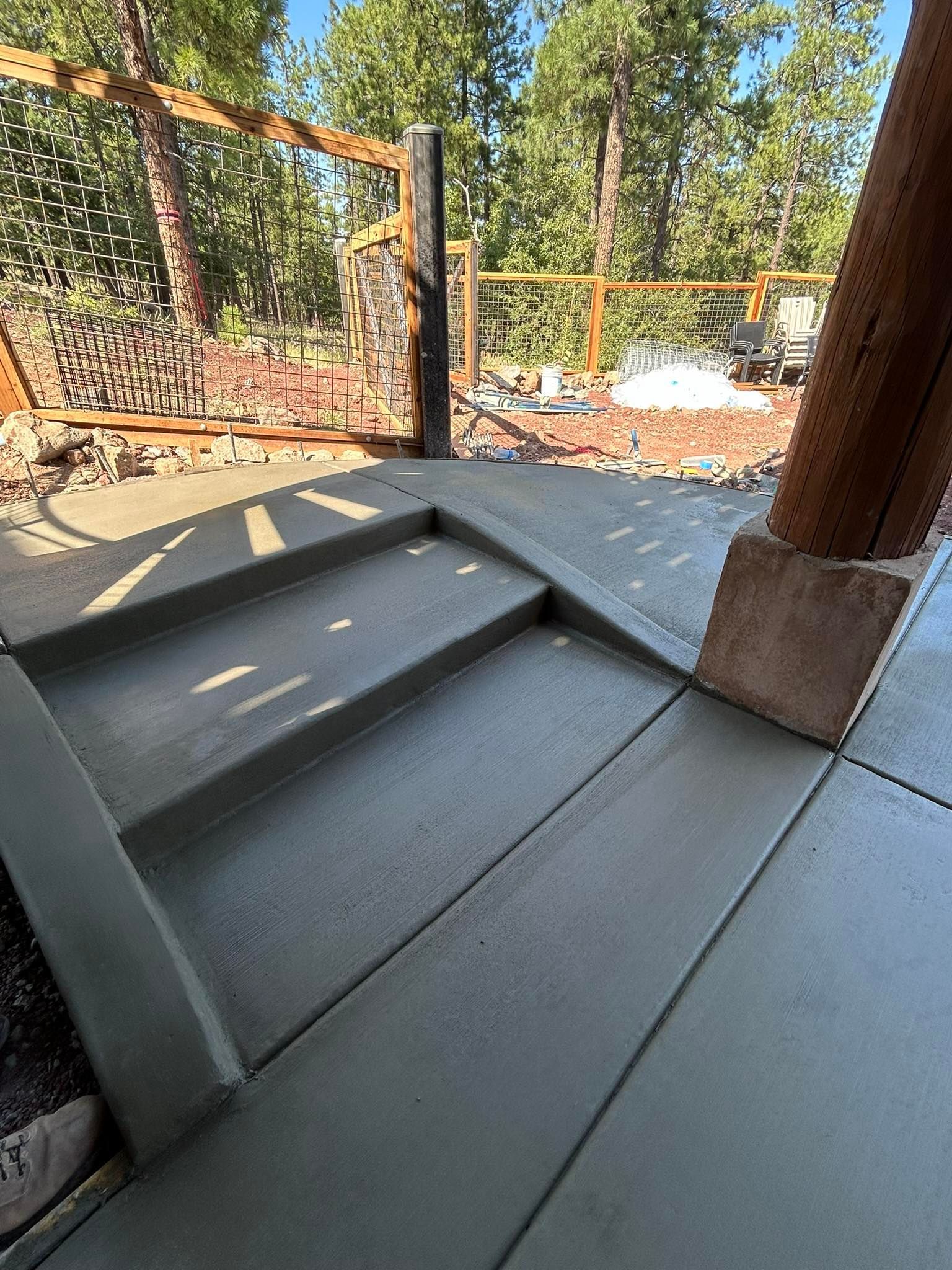 Newly poured concrete patio and steps outside with wooden supports and trees in the background.
