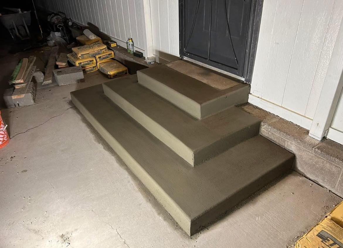 Three newly built concrete steps leading up to a gray door.