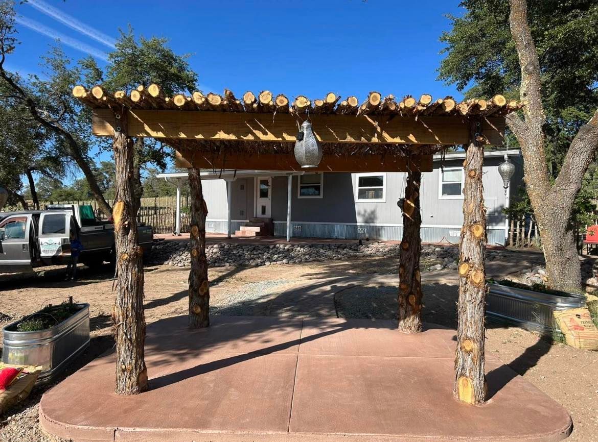 Rustic wooden pergola over a concrete patio; house in the background.