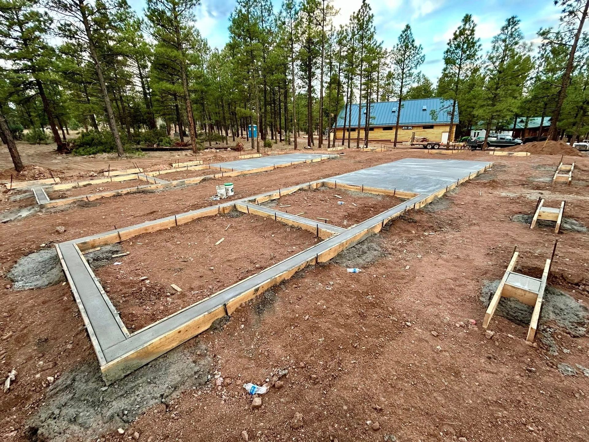 Construction site: concrete foundation forms and a poured concrete slab in a wooded area.