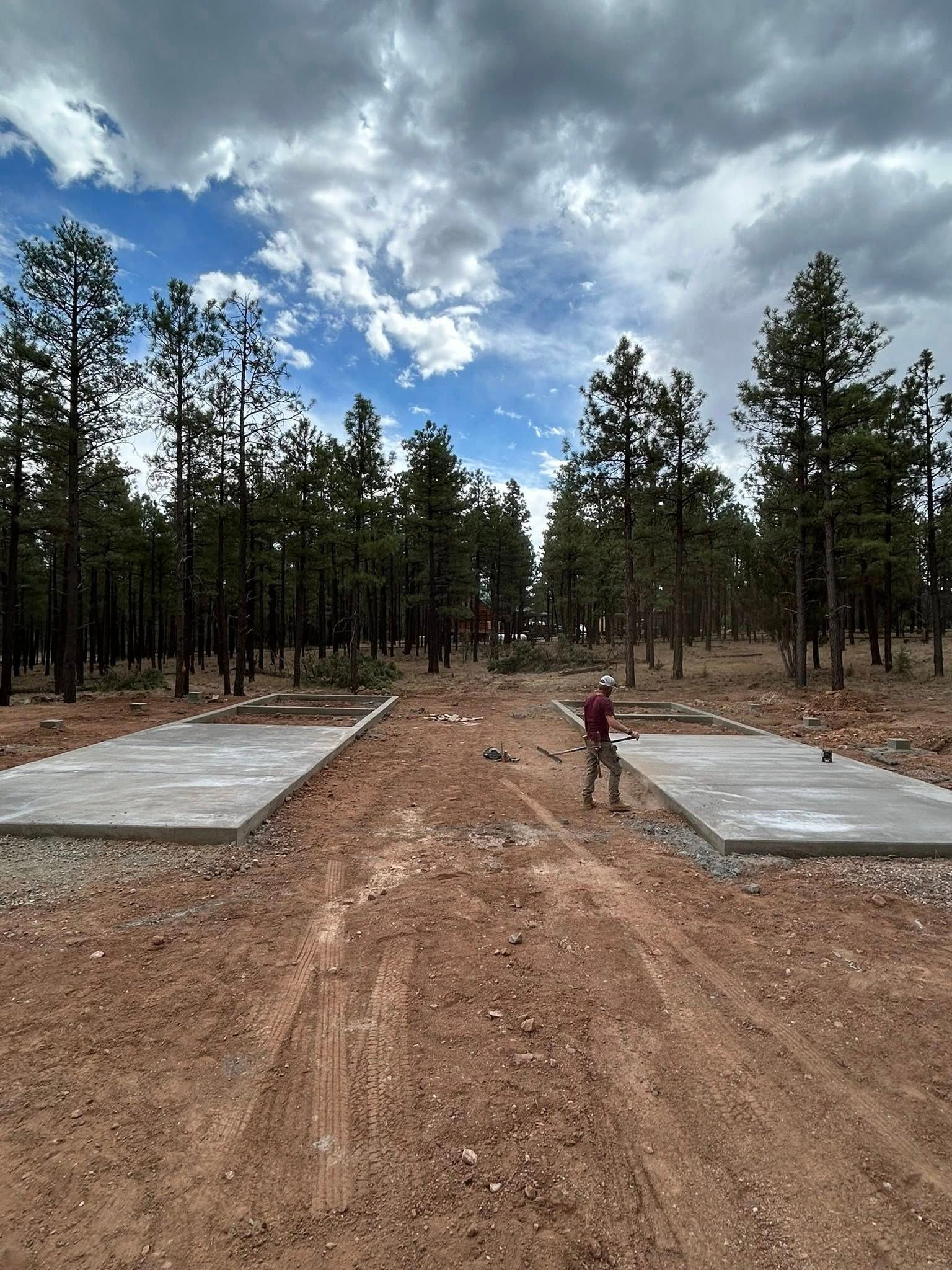 Dirt road through a forest with two concrete pads. Person standing in the center. Cloudy sky.