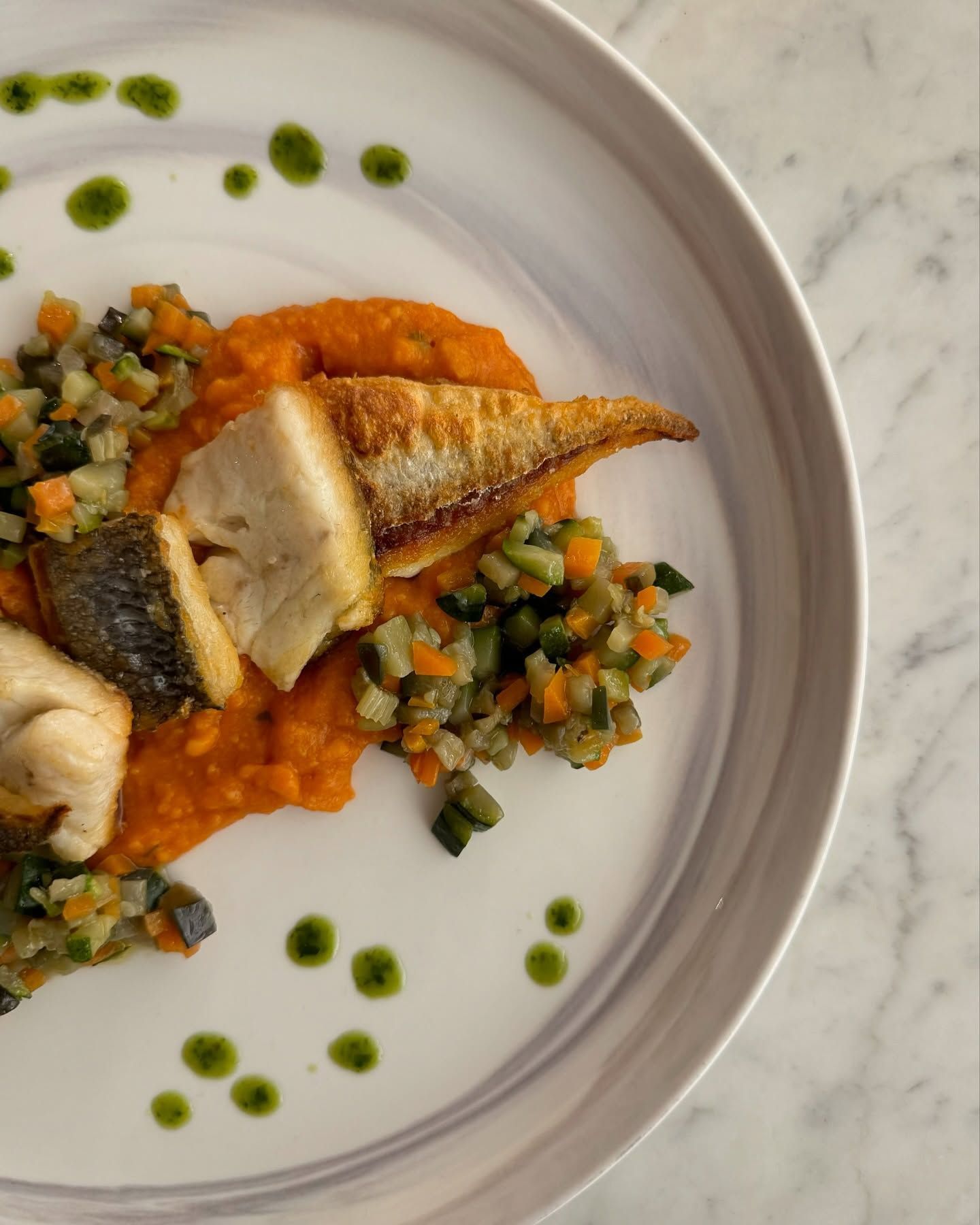 Un piatto bianco con pesce e verdure su un tavolo