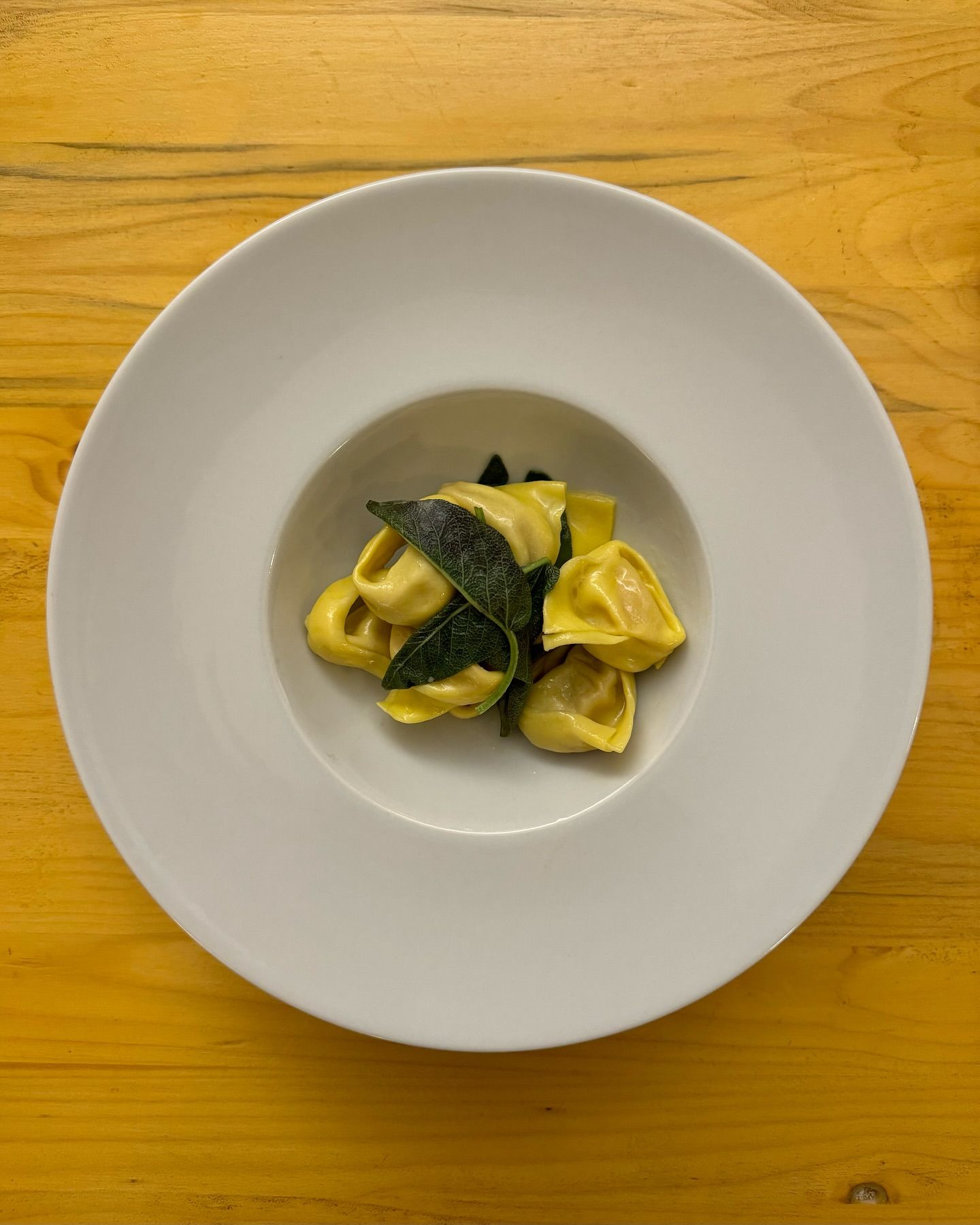 Un piatto bianco con ravioli e spinaci su un tavolo di legno.