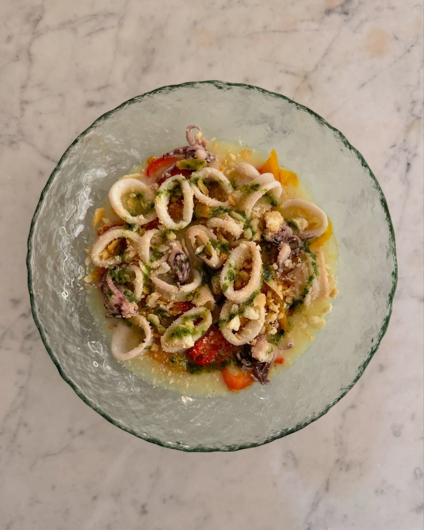 Una ciotola di cibo con calamari e pomodori su un tavolo.