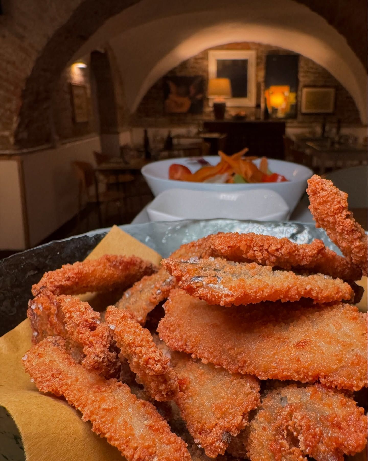 Un piatto di cibo fritto con una ciotola di patatine fritte sullo sfondo