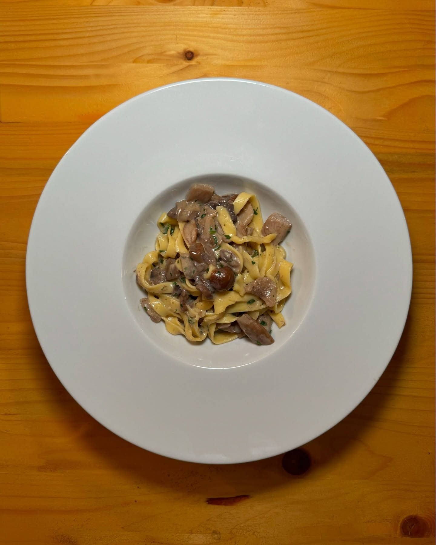 Un piatto bianco con sopra tagliatelle e carne su un tavolo di legno