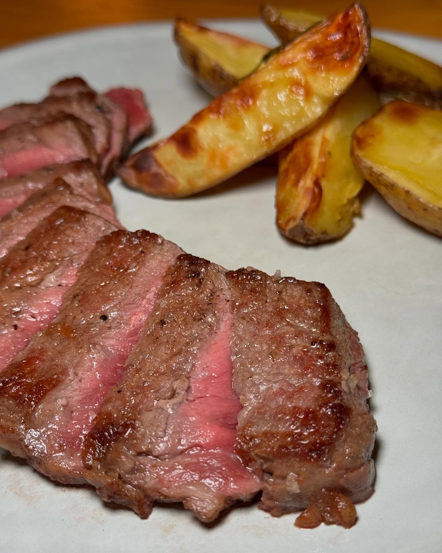 Un piatto bianco con sopra bistecca e spicchi di patate